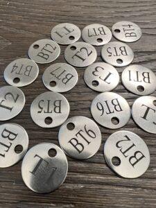 Custom laser-engraved 20-gauge stainless steel tags with letter and number codes, from Signature Laser Designs