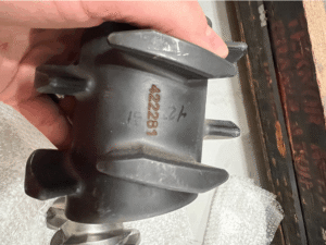 Industrial metal component held by hand showing a permanent laser-engraved serial number marking