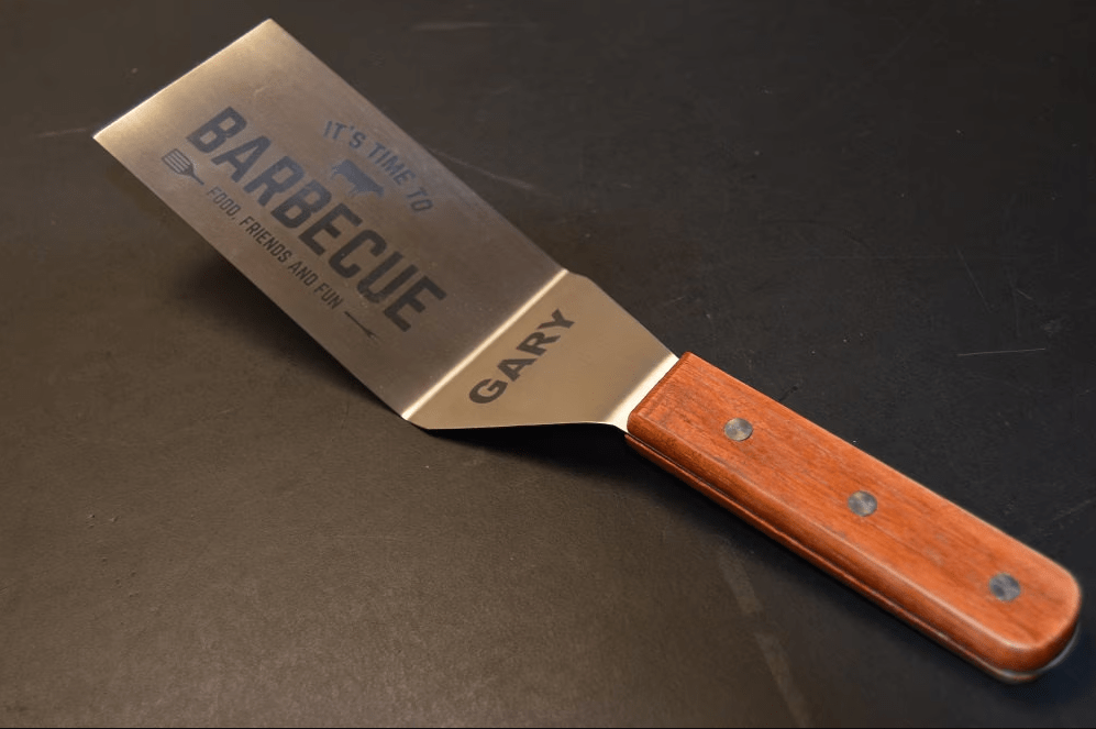 Engraved stainless steel BBQ spatula with wood handle, personalized with the name "Gary" and "It's Time to Barbecue" text — a laser engraved retirement gift for Dad's grill station