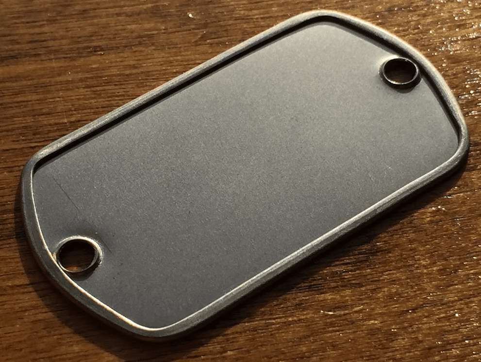 Blank stainless steel two-hole dog tag on wood table, ready for engraving as a custom dog tags veteran gift