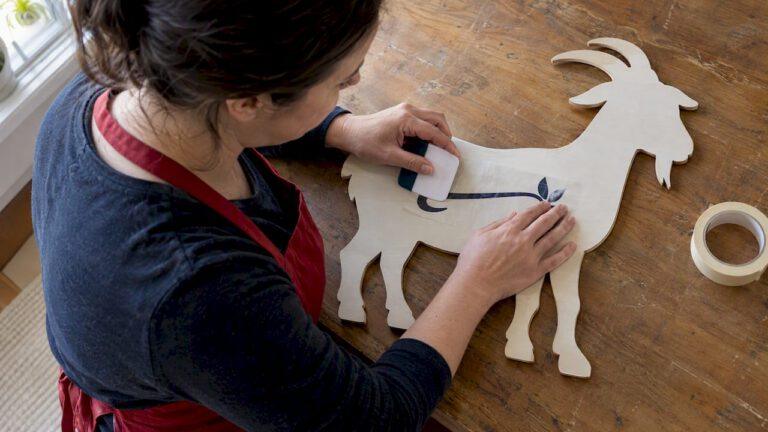 Crafter applying lettering to a wooden goat sign